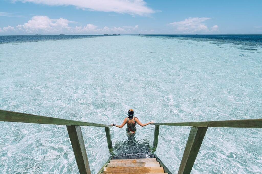 a young woman at the bottom of steps leading from a water villa to the ocean in the Maldives