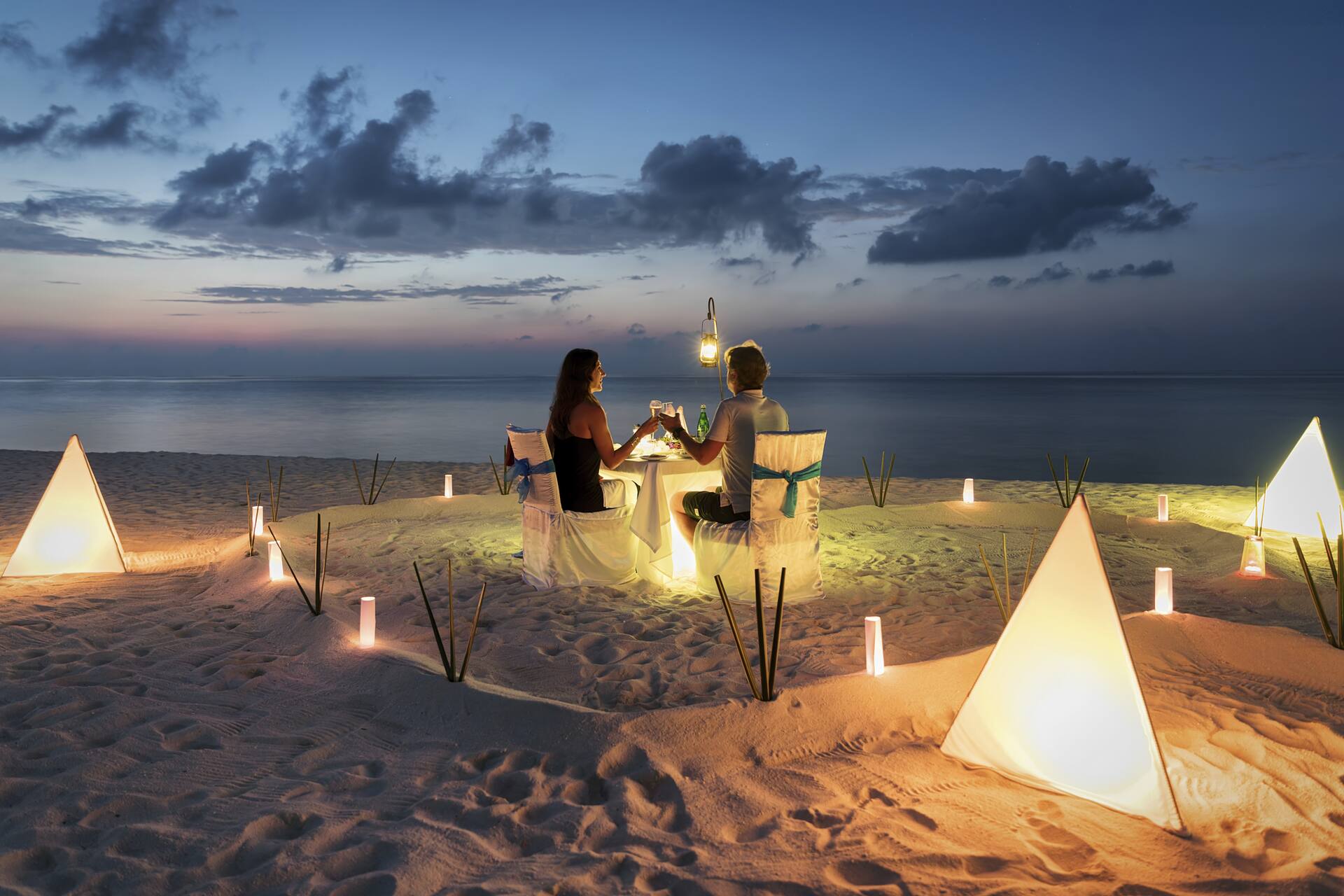 a couple enjoy a candlelit dinner on a tropical beach at sunset in the maldives